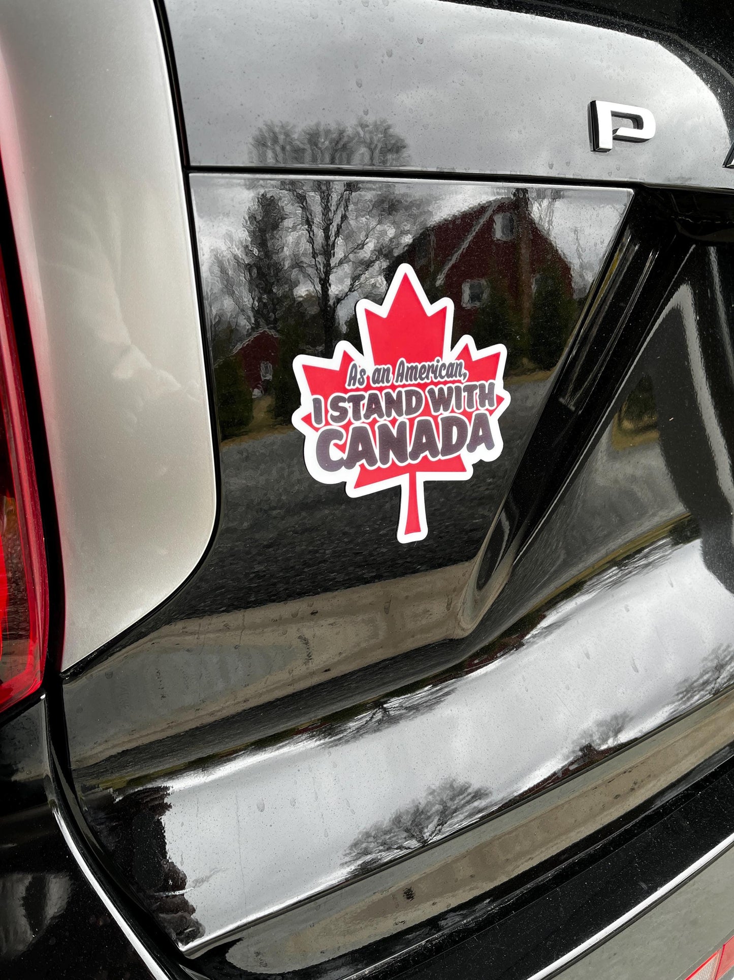 As an American, I Stand With Canada magnet on the back of a car, symbolizing cross-border solidarity and shared democratic values.