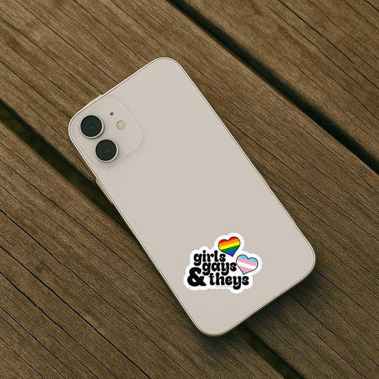 Phone case with 'girls guys & theys' text and rainbow hearts on a wooden surface