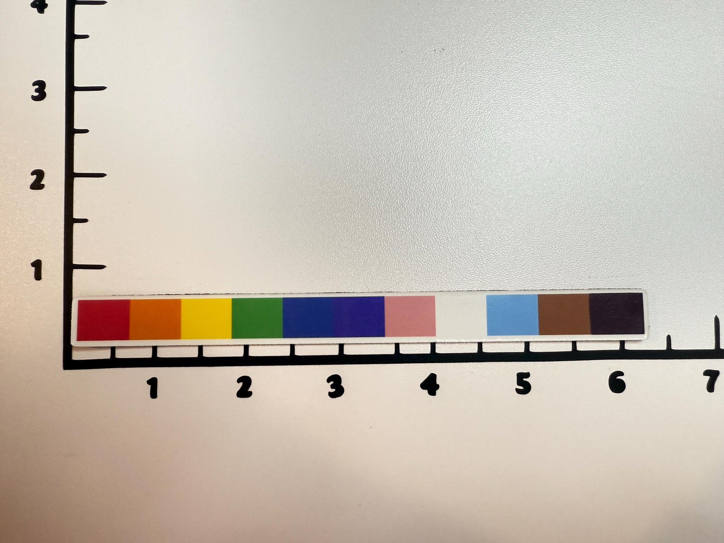 Inclusive rainbow bar magnet placed against a white grid with black markings for scale.