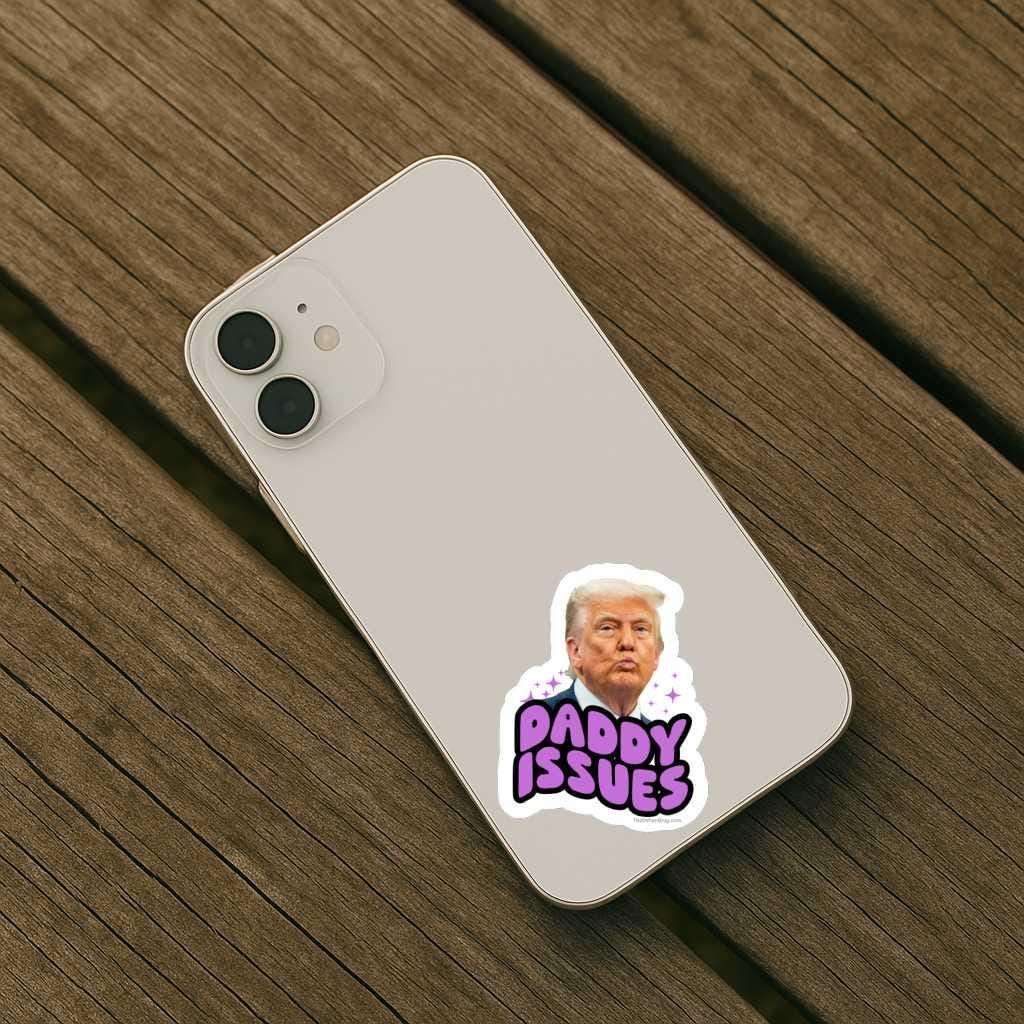Phone with a picture of trump that says 'Daddy Issues' sticker on a wooden surface