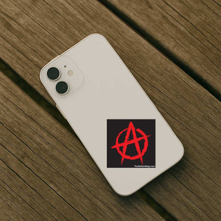 A white smartphone case shown from the back, placed on a weathered wooden surface. The case has a black square sticker near the lower right featuring a red anarchy symbol and small white text reading 'TheDefiantGiftpink.