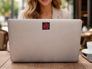 A silver laptop on a wooden table with a round red and white sticker on the lid. 