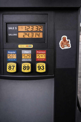 Gas pump display with fuel prices and a sticker of a person on a bear, set against a dark background.