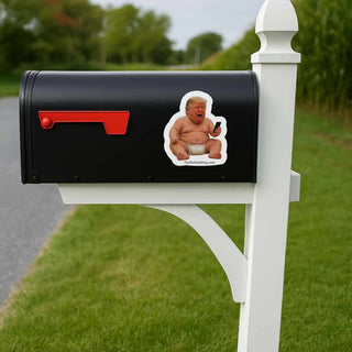 Black mailbox with a sticker of a baby on a phone, mounted on a white post outdoors.
