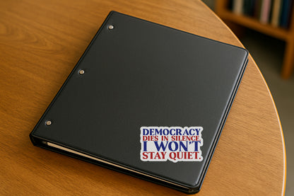 'Democracy Dies in Silence I Won't Stay Quiet' magnet or vinyl decal displayed on a black binder in a library. A bold, high-quality political sticker perfect for cars, laptops, fridges, or toolboxes. Great for activists, protestors, or anyone fed up with fascism.