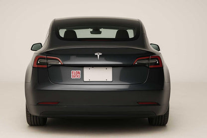 Black Tesla car with a custom license plate on a white background with a sticker that says ELON SUCKS