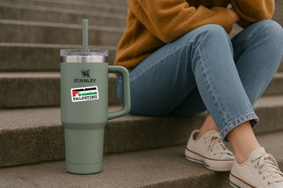 Person sitting on steps with a Stanley tumbler and a sticker on the glass.