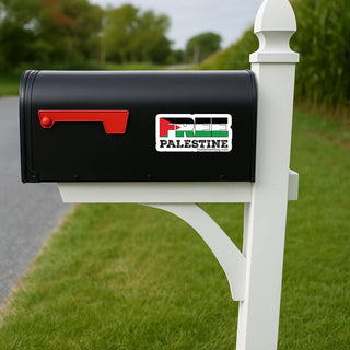 A black mailbox mounted on a white post outdoors, with a Palestine-themed sticker on the front. The sticker features the Palestinian flag colors and the word 'PALESTINE' in bold text.