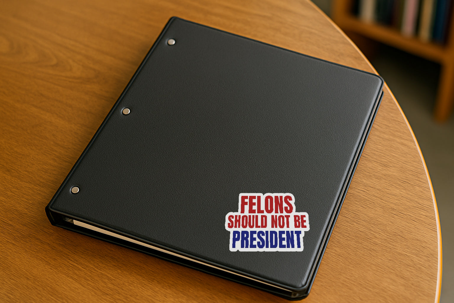Felons Should Not Be President' magnet or vinyl decal displayed on a black binder in a library. A bold, high-quality political sticker perfect for cars, laptops, fridges, or toolboxes. Great for activists, protestors, or anyone fed up with fascism.