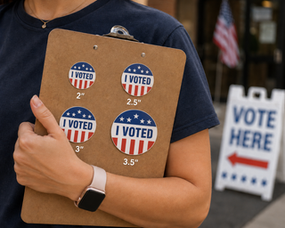 A person holds a brown clipboard with four round 'I VOTED' stickers in different sizes (2", 2.5", 3", 3.
