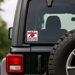 Funny MAGA Daddy Issues anti-Trump sticker on the rear window of a black Jeep Wrangler beside the spare tire. Square red and blue political decal reads Telling the World You Have Daddy Issues One Red Hat at a Time.