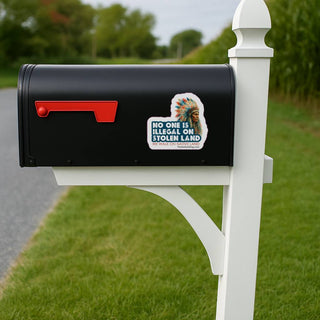 Black mailbox with a sticker on a white post in a grassy area.