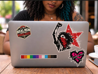 Real Men Support Women’s Rights sticker on laptop with feminist protest stickers in creative café workspace.