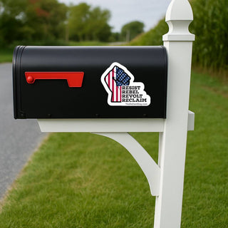 Black mailbox with a sticker on a white post in a grassy area.