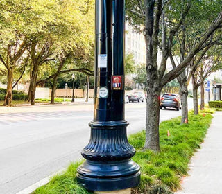 Black street lamp post on a city street with trees and cars in the background