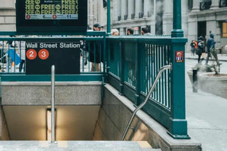 Subway entrance with 'Wall Street Station' sign and people walking by.
