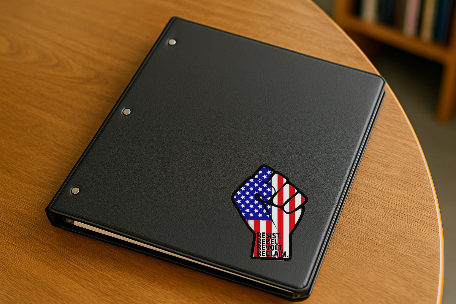 Resist Rebel Revolt Reclaim' magnet or vinyl decal displayed on a black binder in a library. A bold, high-quality political sticker perfect for cars, laptops, fridges, or toolboxes. Great for activists, protestors, or anyone fed up with fascism.
