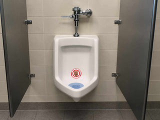 Trump urinal target sticker displayed inside a public restroom urinal as a humorous political bathroom decal.
