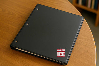 Black notebook with 'Abolish ICE' on a wooden surface
