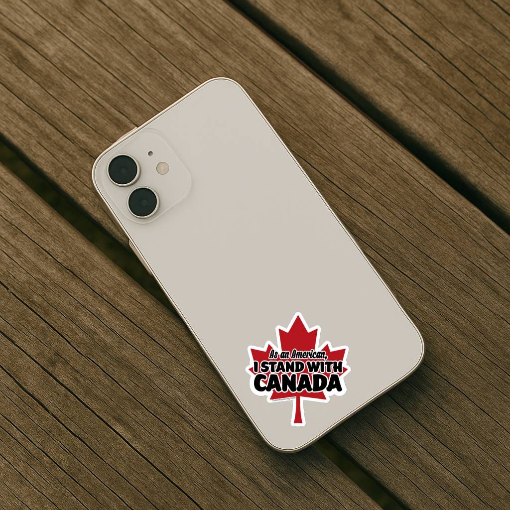 As an American I Stand With Canada maple leaf support sticker applied to the back of a light-colored smartphone on a wooden surface.