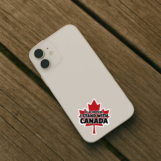 As an American I Stand With Canada maple leaf support sticker applied to the back of a light-colored smartphone on a wooden surface.
