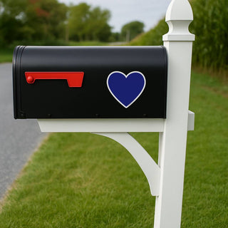 Black mailbox with a blue heart on a white post in a grassy area.