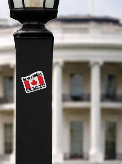 Dear Canada We Hate Him Too anti Trump protest sticker on black lamp post with White House background, Canadian flag political vinyl decal, progressive activist resistance bumper sticker, outdoor street statement design