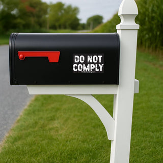 Black mailbox with 'DO NOT COMPLY' text on a white post in a grassy area.