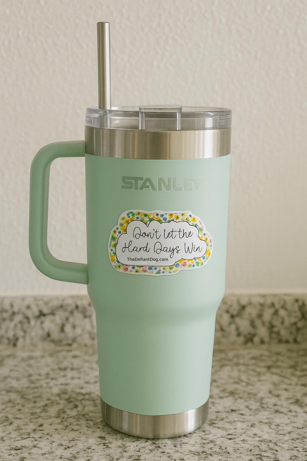 stanley tumbler with a sticker that says don't let the hard days with and thedefiantdog.com with a yellow floral border.