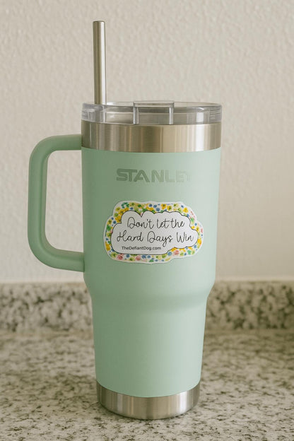 stanley tumbler with a sticker that says don't let the hard days with and thedefiantdog.com with a yellow floral border.