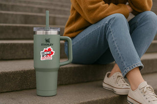 Person sitting on steps with a Stanley tumbler and a sticker on the tumbler.