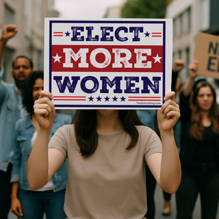 Person holding an Elect More Women political protest sign at a rally, featuring a red white and blue vintage election campaign-style design.