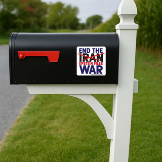A black mailbox on a white post with a red flag, placed outdoors on grass beside a road. A white sticker on the mailbox reads “END THE IRAN EPSTEIN FILES WAR” with red and blue text.