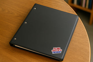 Felons Should Not Be President vinyl sticker on black binder, political protest decal with red white and blue text activist statement sticker