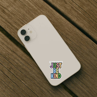 White iPhone on a wooden surface with a ‘For fuck’s sake just be kind’ sticker on the back.