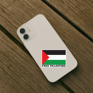 A white smartphone lying on a rustic wooden plank surface, featuring a Palestine flag sticker with the text 'FREE PALESTINE' printed below it.