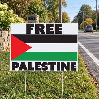 A yard sign on metal stakes in a grassy roadside setting, printed with the words “FREE PALESTINE” over the Palestinian flag design.