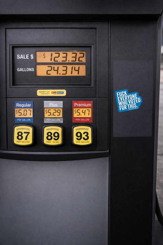 Fuel pump display with prices and a humorous sticker on a black background