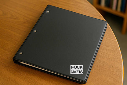 Black notebook with 'FUCK NAZIS' text on a wooden surface