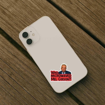 Phone case with a sticker of a man and text 'WHO MICROWAVED MEL GIBSON?' on a wooden surface