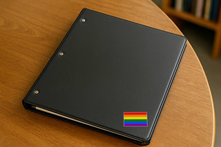 Black notebook with a rainbow sticker on a wooden surface