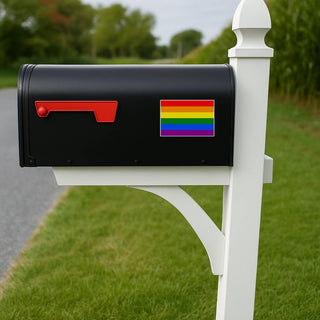Black mailbox with a rainbow flag sticker on a white post in a grassy area.