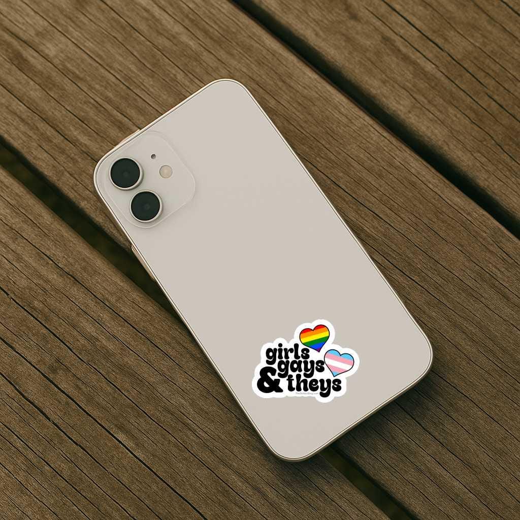 Phone case with 'girls guys & theys' text and rainbow hearts on a wooden surface