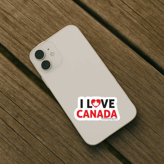 A white smartphone case with a 'I LOVE CANADA' graphic sticker, shown from an overhead angle on a dark wood plank surface.