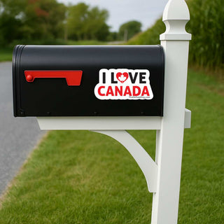 A black mailbox mounted on a white post outdoors, with a red flag and a white sticker that reads “I LOVE CANADA” on the side.