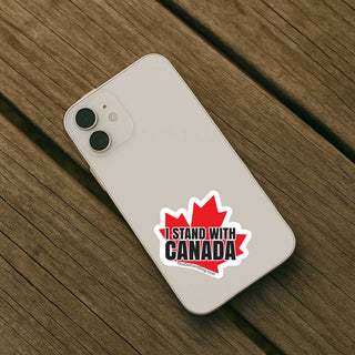 A white smartphone case shown from the back on a wooden plank surface, featuring a red maple leaf graphic with the text 'I STAND WITH CANADA' and a small website URL.