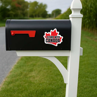Black mailbox with a political sticker on a white post in a grassy area.