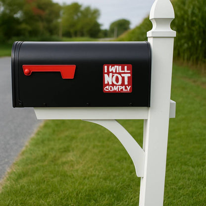 Black mailbox with 'I WILL NOT COMPLY' sticker on a white post, outdoors.