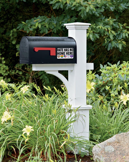 Black mailbox with a 'Hate Has No Home Here' sticker on a white post, surrounded by greenery.
