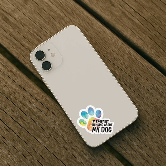 Phone case with 'I'm Probably Thinking About My Dog' sticker on a wooden surface